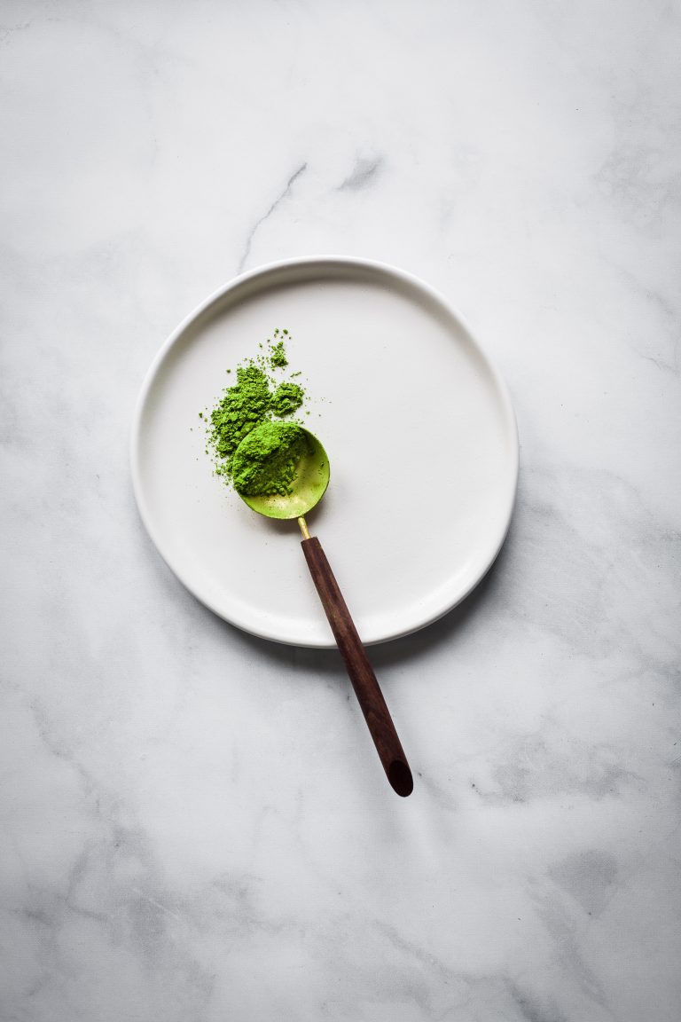 overhead view of a spoon of matcha tea on a white place on a marble surface.