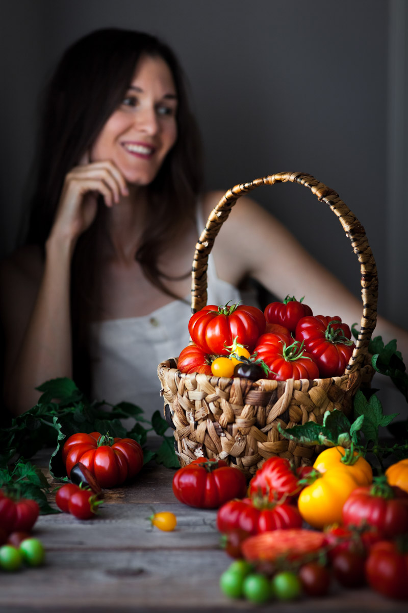 Woman seated behind a table covered with a variety of tomatoes.