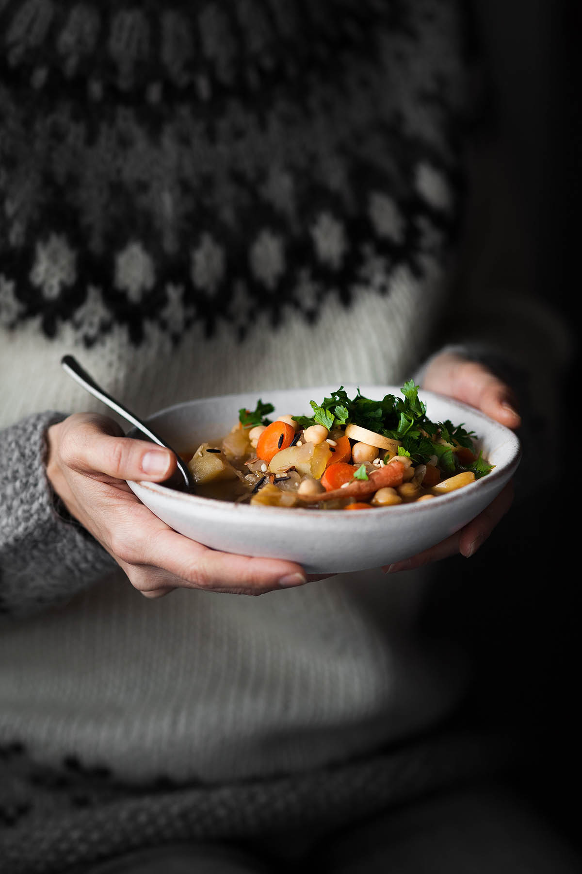 Woman in a thick sweater holding a bowl of vegetable soup.