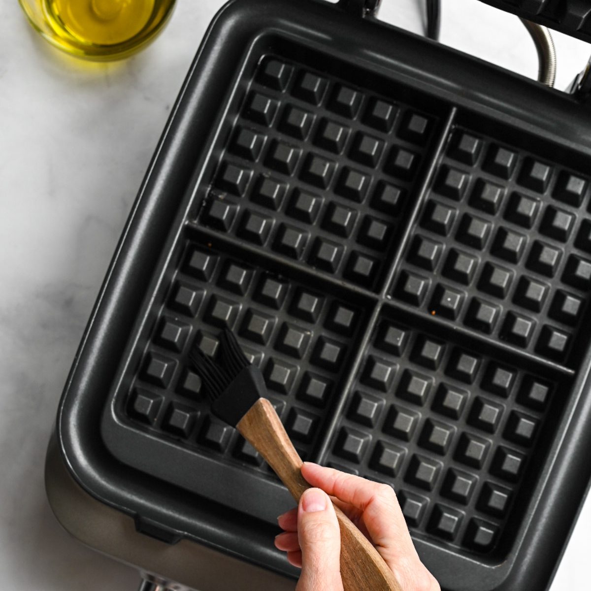 a person brushing oil into a waffle iron.