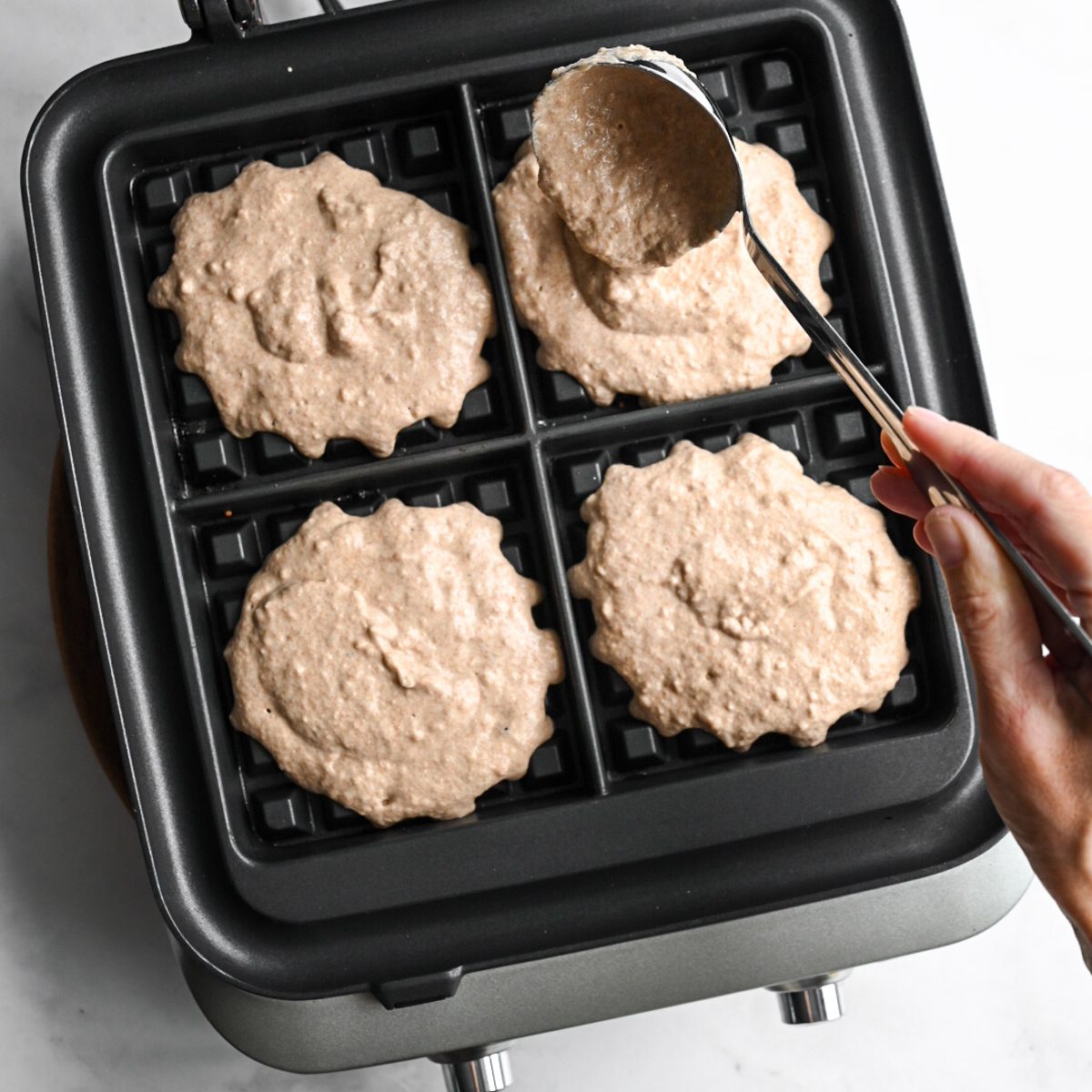 a person portioning waffle batter with a ladel into a waffle iron.