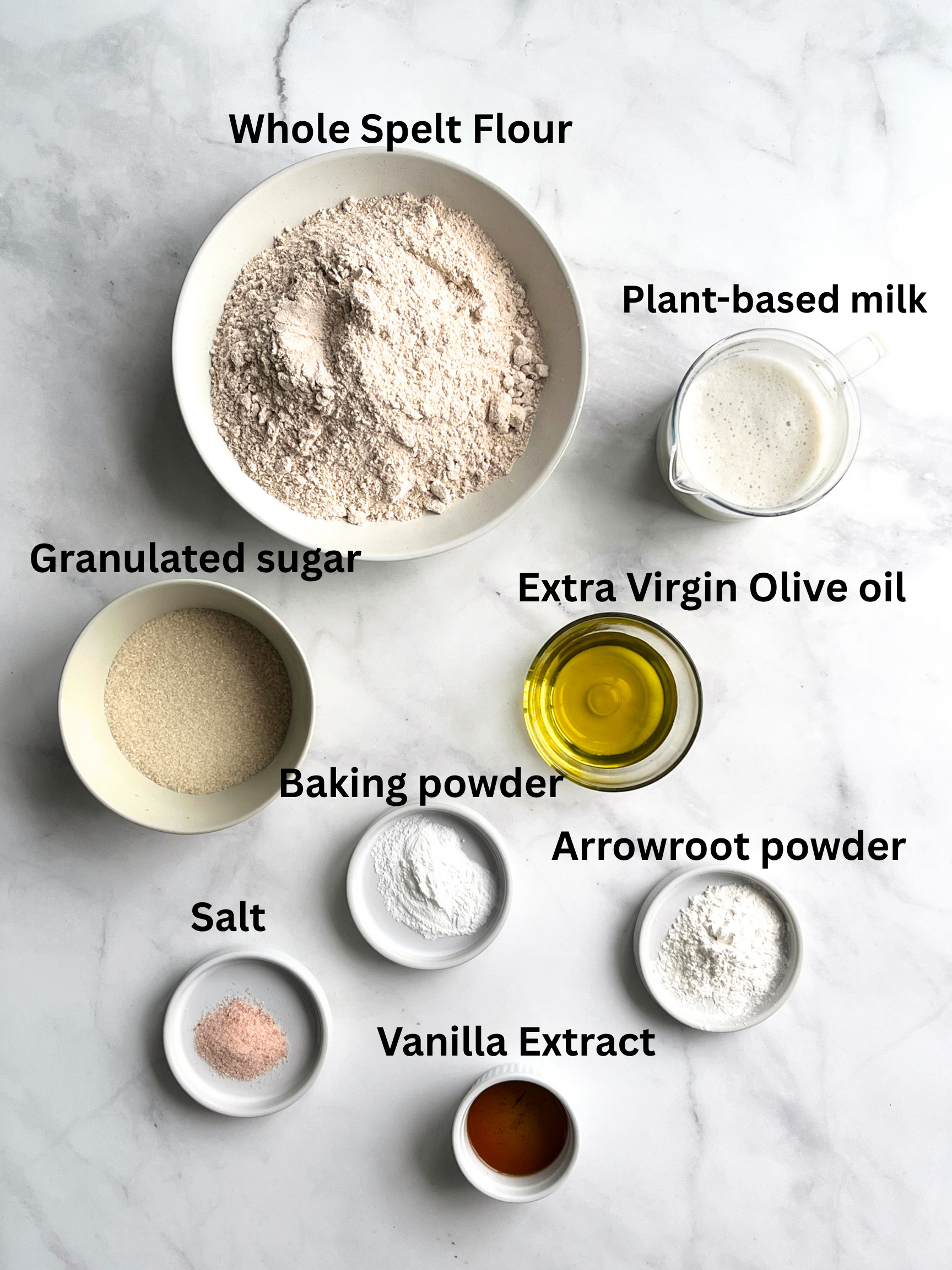overhead photo of various ingredients used to make vegan spelt waffles clustered on a white marble surface with labels for each.