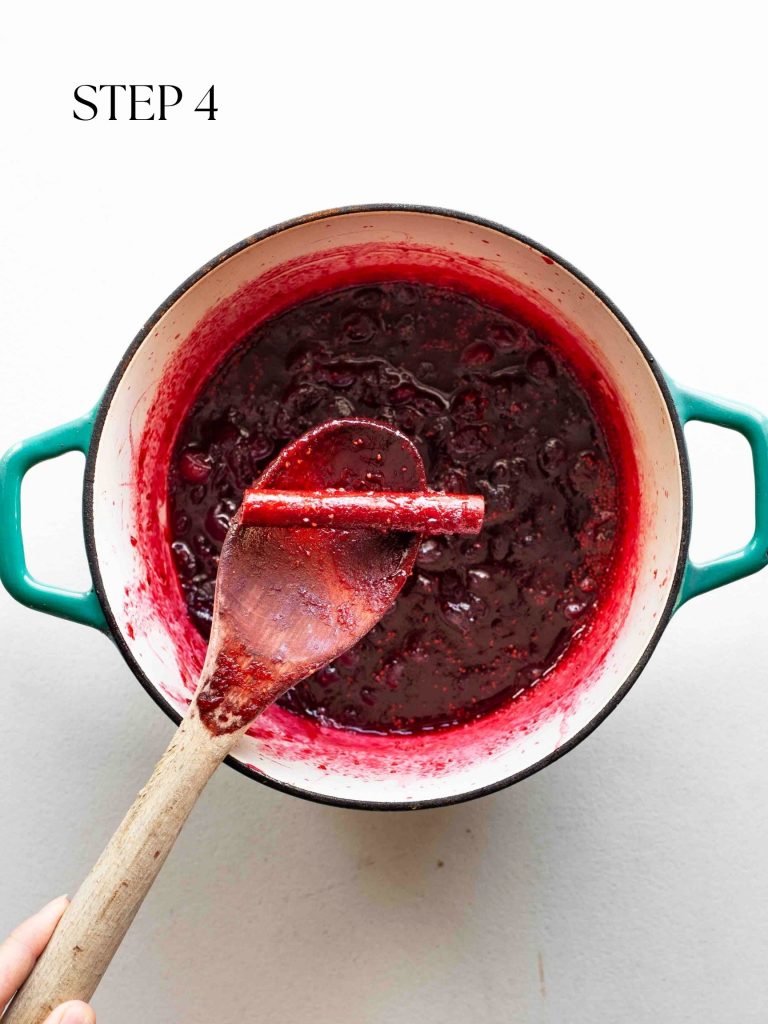 a wooden spoon removing a cinnamon stick from a pot of cranberry sauce with text overlay "step 4".