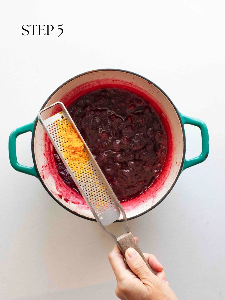 a hand holding a zester of orange peel over a pot of cranberry sauce with text overlay "step 5".
