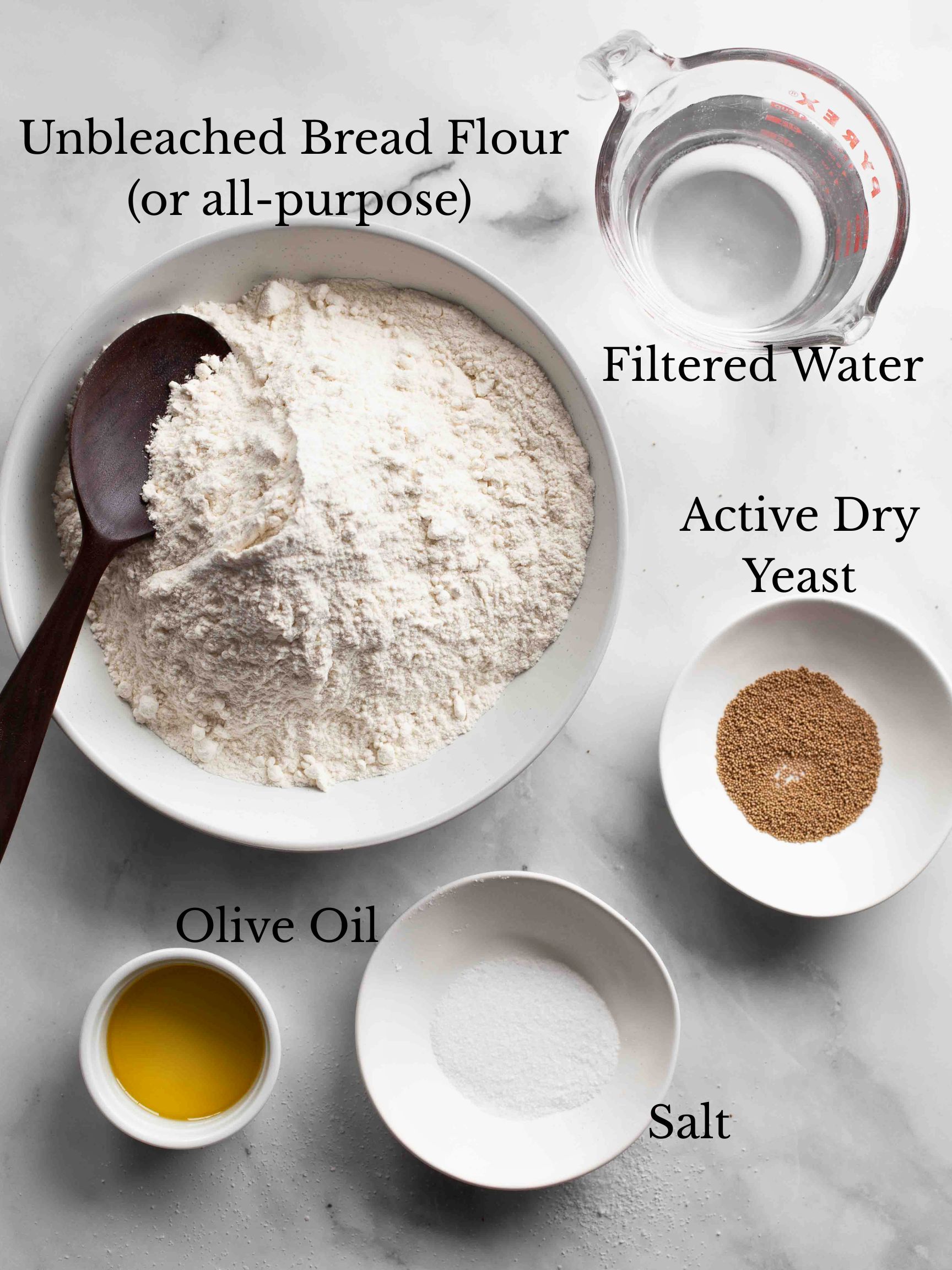 The various ingredients used to make a fougasse bread recipe on a stone surface with labels for each.