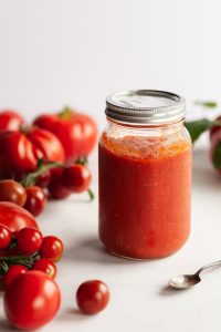 a jar of marinara sauce on a white surface with fresh tomatoes around it.