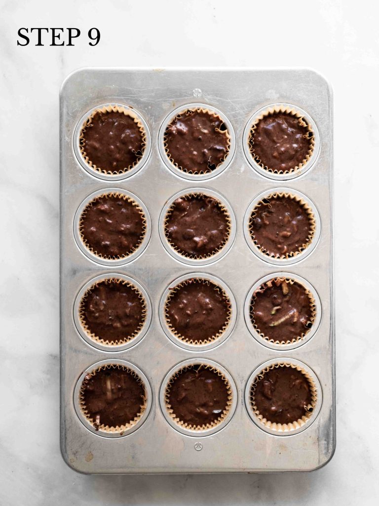 A muffin pan filled with chocolate zucchini muffin batter on a marble surface.