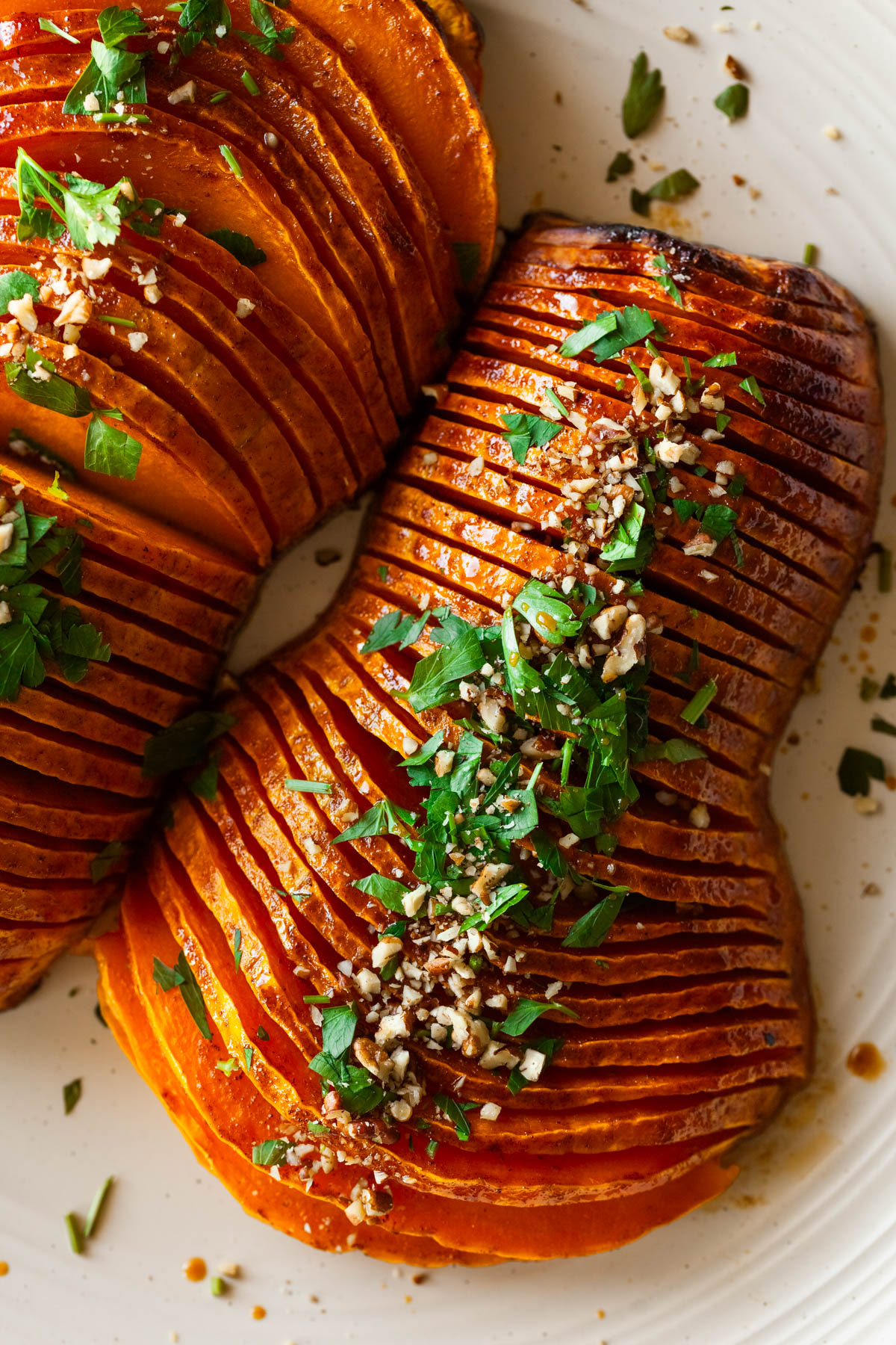 two hasselback butternut squash halves on a platter with parsley leaves, and a knife and serving spoon.
