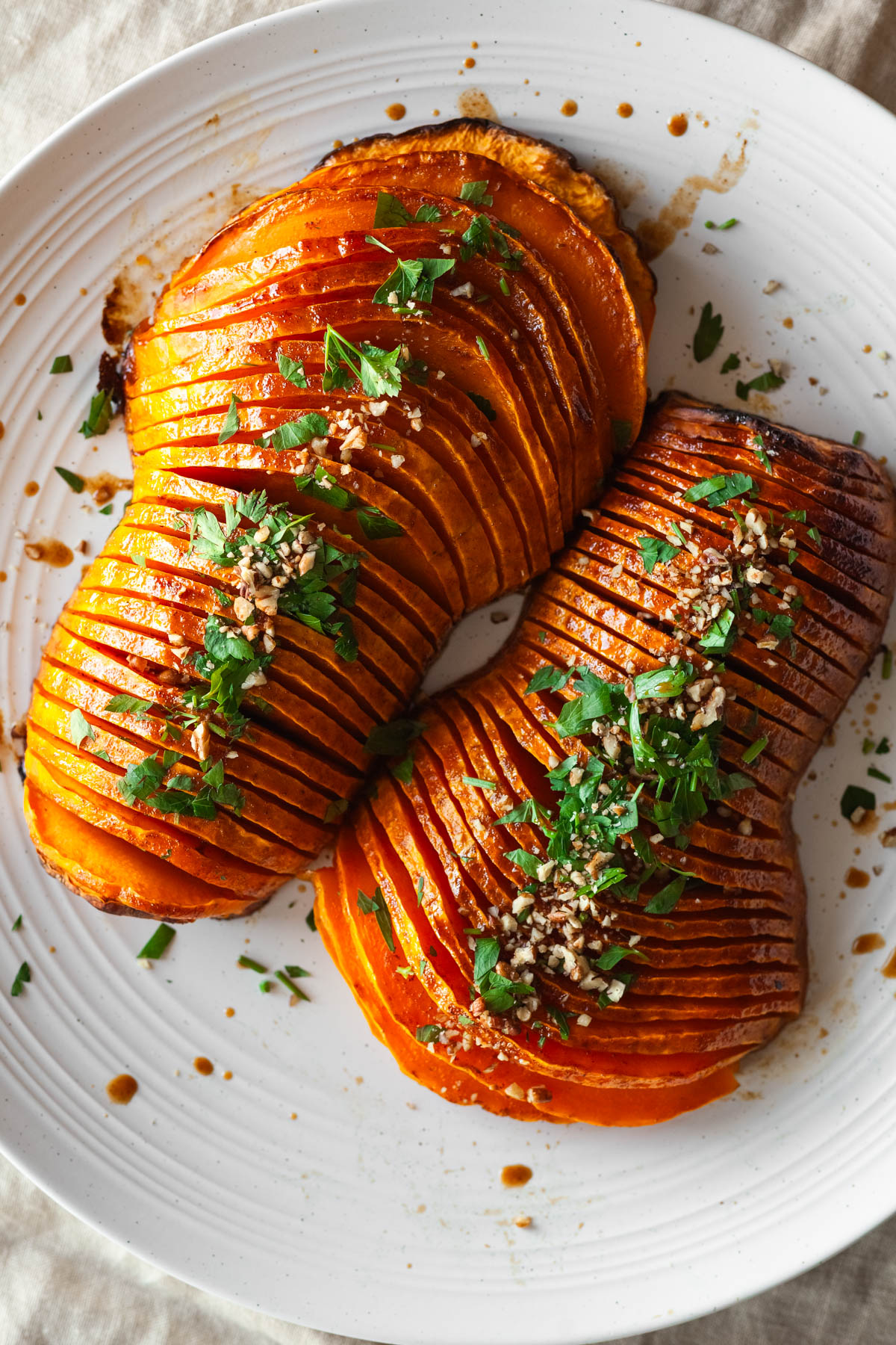 two hasselback butternut squash halves on a platter with parsley leaves, and a knife and serving spoon.