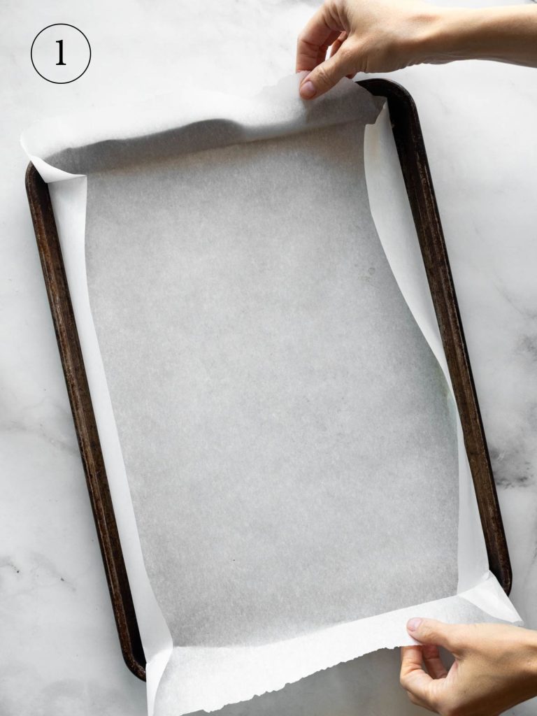 a cook placing parchment paper on a baking sheet.
