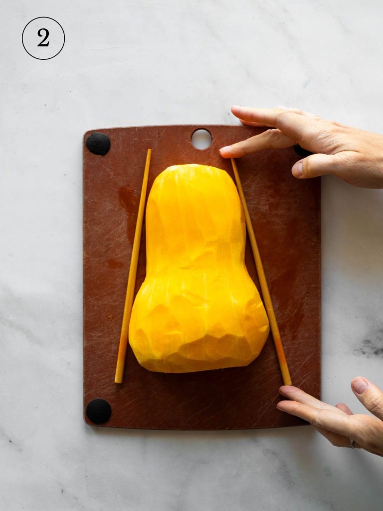 a cook placing chopsticks on either side of a butternut squash half on a cutting board.