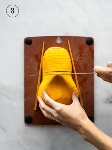 a cook slicing a butternut squash half on a cutting board with two chopsticks on either side of the squash.