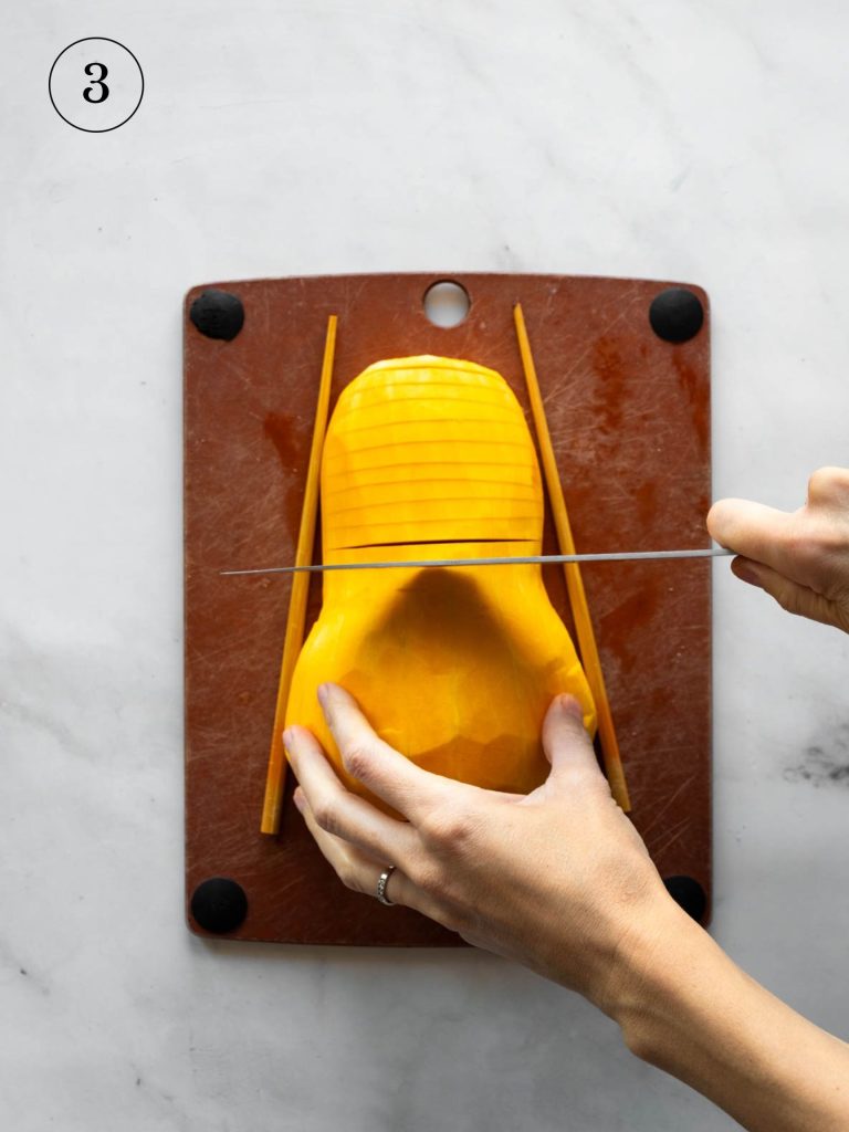 a cook slicing a butternut squash half on a cutting board with two chopsticks on either side of the squash.
