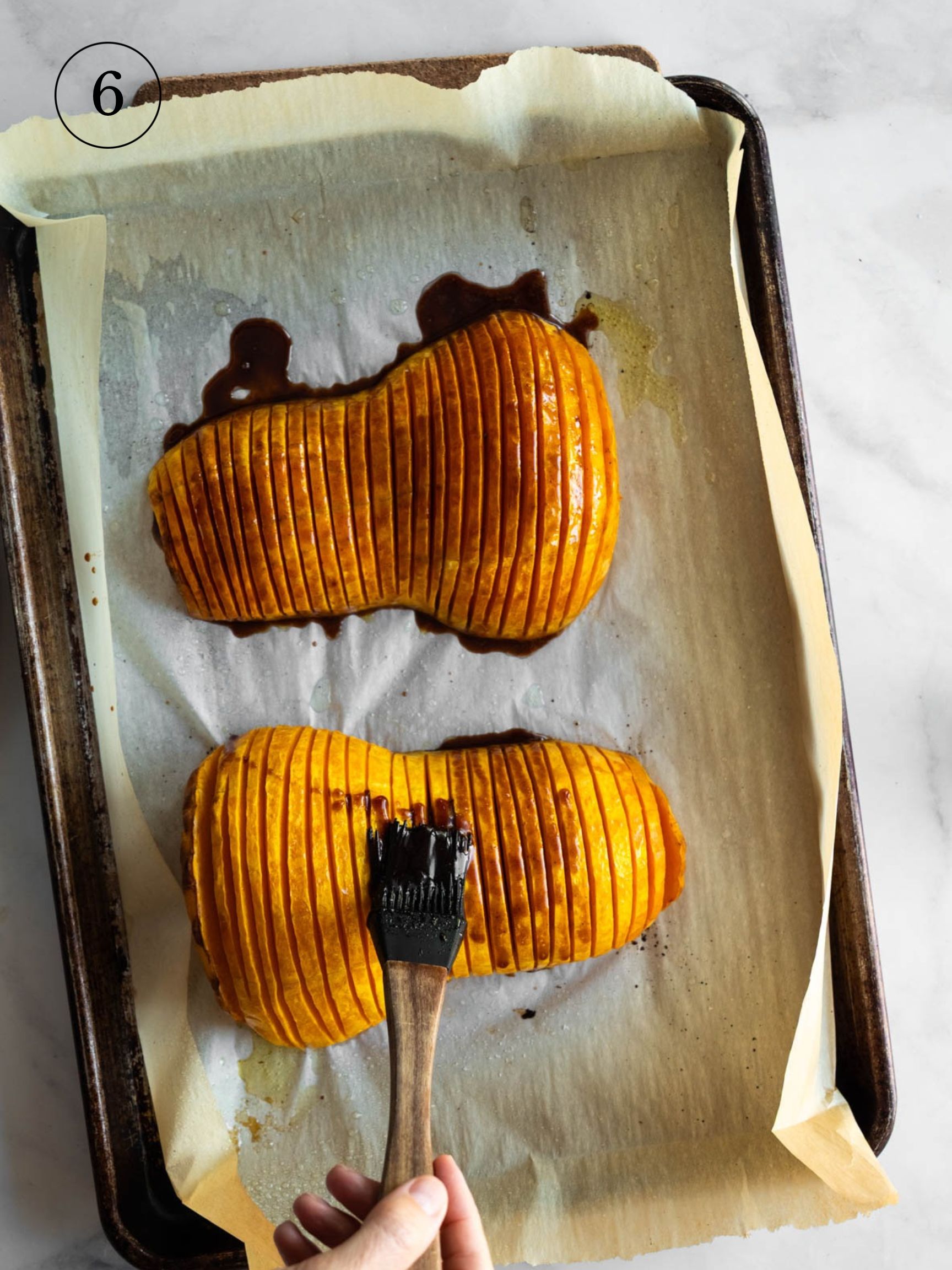 basting the top of two hasselback squash on a baking tray with parchment paper.