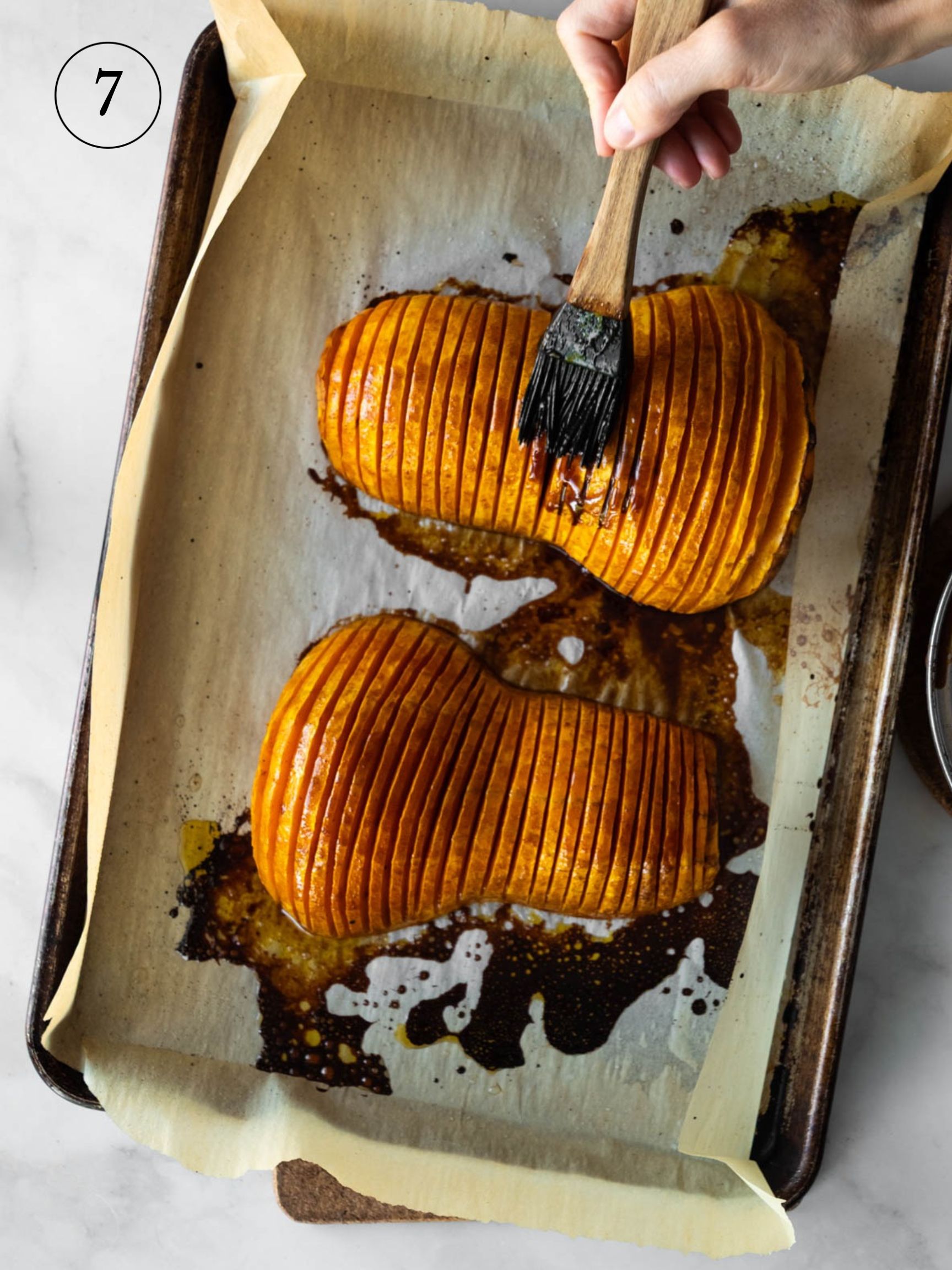 basting the top of two hasselback squash on a baking tray with parchment paper.