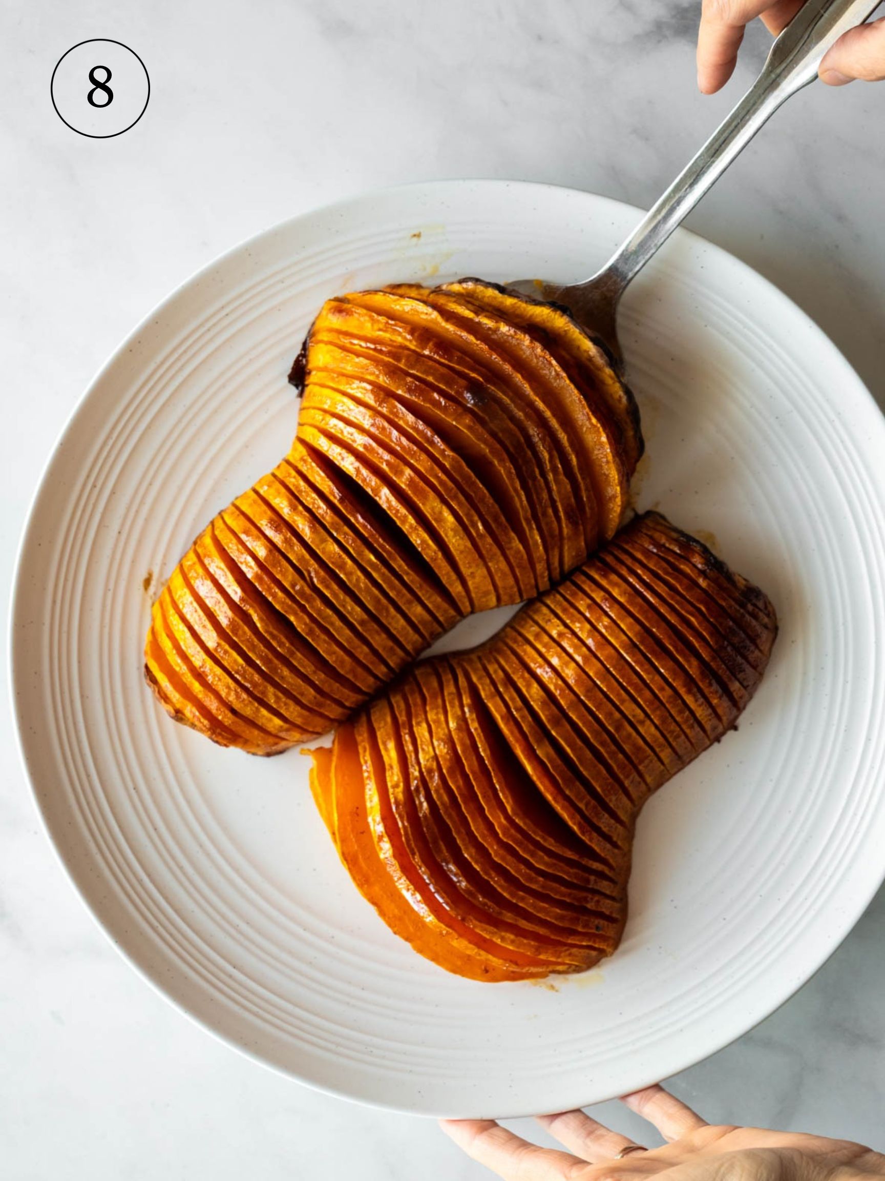 hands using a spatula to place baked hasselback squash on a serving plate.